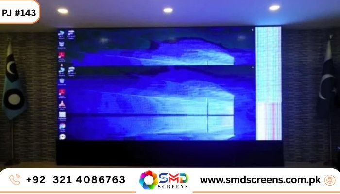 A very large indoor LED video wall displaying a blue Windows desktop screen with icons, flanked by two flags on poles.