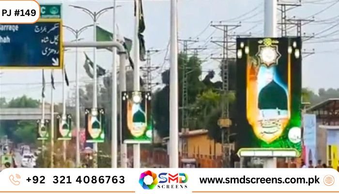 Multiple vertical outdoor LED screens mounted on poles along a busy street, displaying a religious/spiritual graphic featuring a green dome and calligraphy.