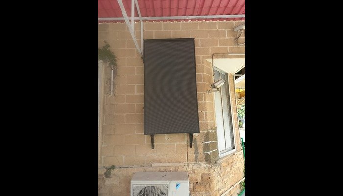 Outdoor SMD LED screen (3x6 size) installed on a brick wall at Dow Ujah Karachi, mounted under a red roof with supporting brackets and visible wiring near an air conditioning unit.