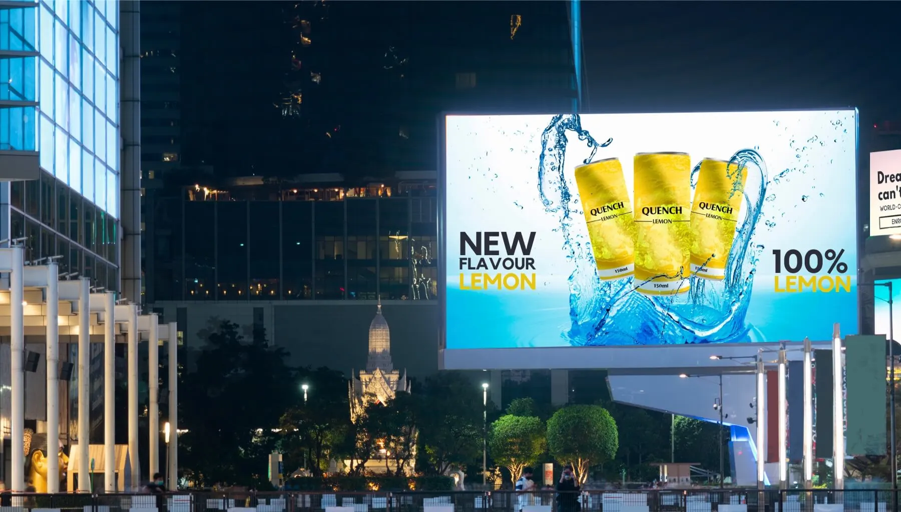 Digital billboard at night showing “Quench” lemon drink ad with cans splashing in water and text “100% Lemon.